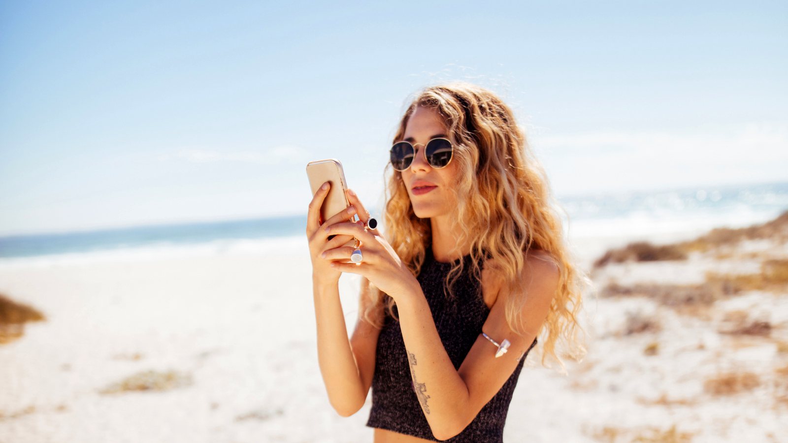 Traveler checking her phone on the beach next to a van