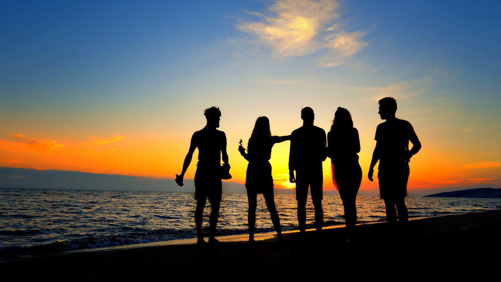 Friends silhouetted on the beach at sunset